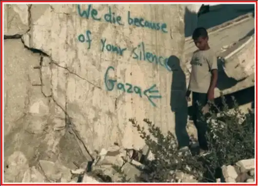 Un enfant se tient devant un bâtiment en ruine et il est écrit sur le mur en anglais 'Nous mourons à cause de votre silence Gaza'